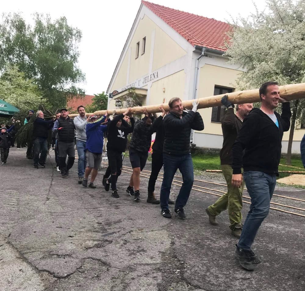 Skupina mužů nese májku před budovou Hostince U Jelena