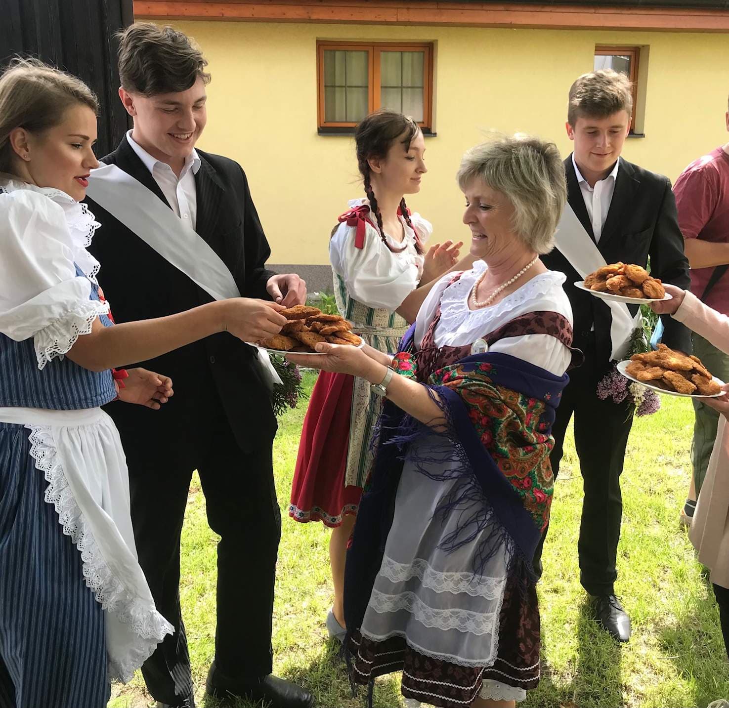 Skupina lidí v krojích a oblecích si podává talíře s jídlem
