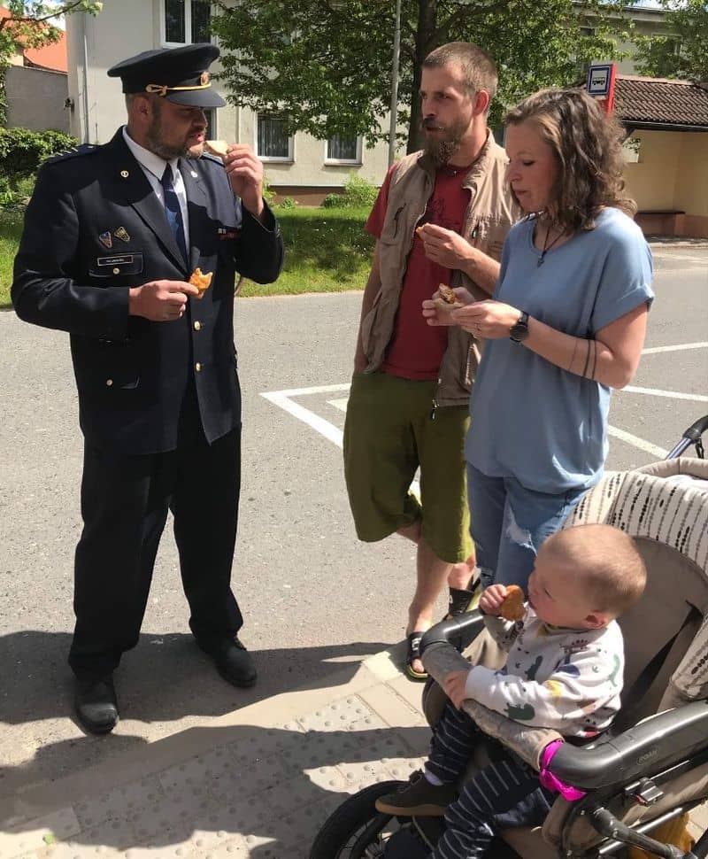 Muž v uniformě, muž, žena a dítě v kočárku jedí pečivo
