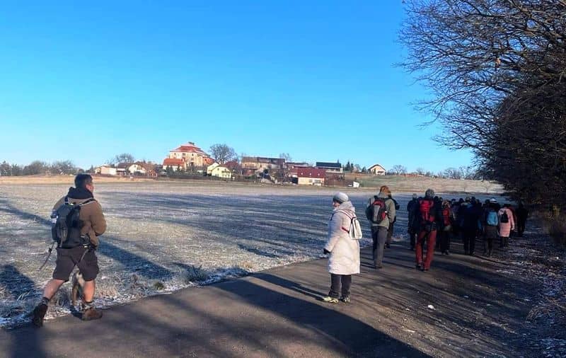 Skupina lidí na procházce po zasněžené cestě s výhledem na vesnici