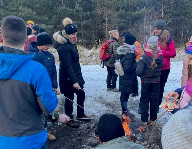 Skupina lidí a dětí opéká buřty na ohni v zasněžené krajině