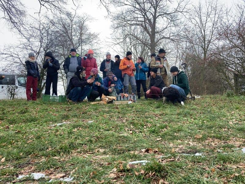 Skupina lidí a pes v přírodě, někteří sedí u ohně