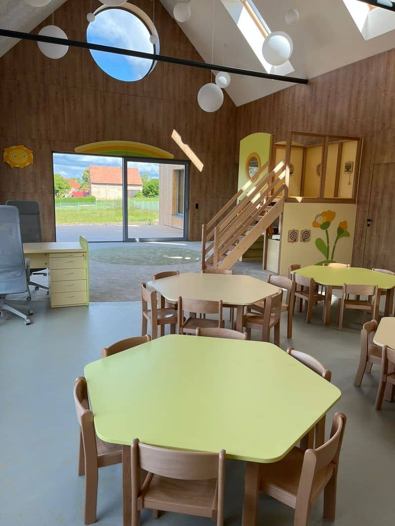Jídelní část herny se stolky a dětskými židličkami, v pozadí schodiště na patro