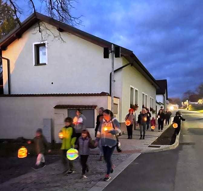 Skupina lidí s lucernami jde po ulici za soumraku