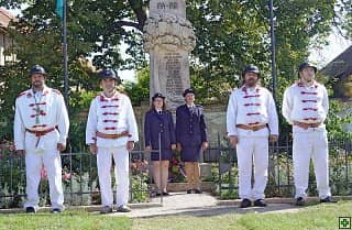 Skupina mužů v krojích a žen v uniformách před pomníkem
