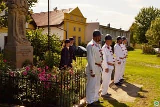 Skupina mužů v historických uniformách stojí u pomníku
