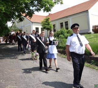 Průvod lidí v krojích a oblecích, v čele muž v uniformě