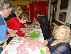 Skupina lidí u stolu s hracími kartami, žena v popředí se dívá do objektivu