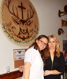 Dvě ženy před dřevěným obrazem jelena, jedna v hasičské uniformě