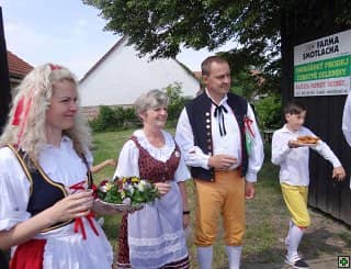 Tři dospělí v krojích a chlapec s talířem jídla venku