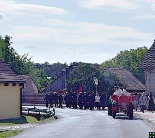 Průvod lidí v historických kostýmech s traktorem na silnici v obci