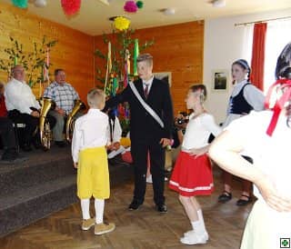 Děti tančí v sále, v pozadí hudebníci a májka