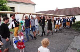 Skupina mužů v krojích i civilu nese májku, v popředí dvě malé děti