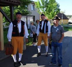 Tři muži v krojích a dvě ženy na ulici před domem
