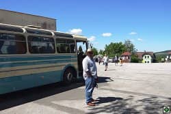 Muž stojí u historického autobusu, v pozadí další lidé a domy