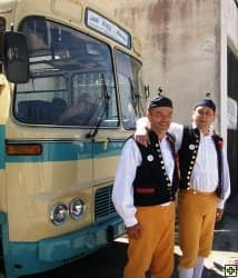 Dva muži v krojích stojí před historickým autobusem