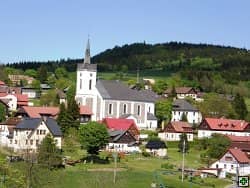 Kostel a domy v obci pod zalesněným kopcem