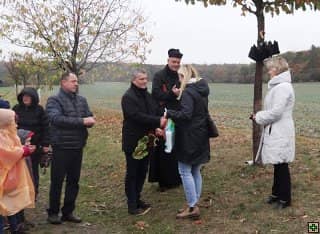 Skupina lidí s knězem venku, muž podává ženě kytici