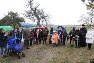 Skupina lidí s deštníky na louce, vpravo kněz