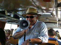 Muž v klobouku a slunečních brýlích mluví do megafonu v autobuse