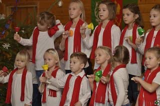 Skupina dětí v bílých tričkách a červených šálách hraje na zvonečky
