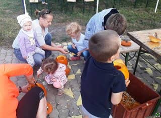 Dospělí a děti dlabou dýně na zemi a u stolu