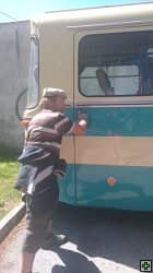 Muž v kšiltovce čistí bok historického autobusu