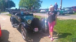 Žena v růžových kalhotách stojí u historického automobilu