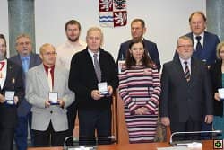 Skupina lidí s medailemi před znakem obce