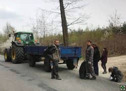 Skupina lidí s traktorem a přívěsem sbírá odpadky u silnice