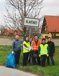 Skupina lidí s pytli na odpadky u cedule Hlavenec