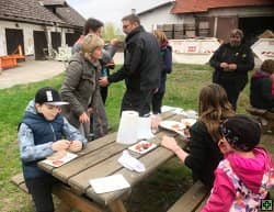 Skupina lidí u stolu venku, v pozadí hospodářské budovy