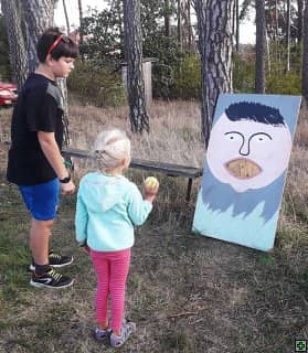 Děti hrají venkovní hru s míčkem a terčem s obličejem
