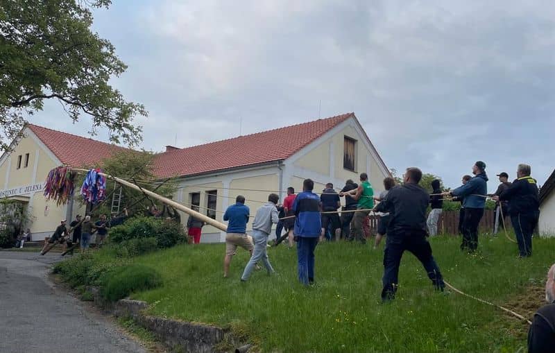 Skupina mužů staví májku před budovou hostince