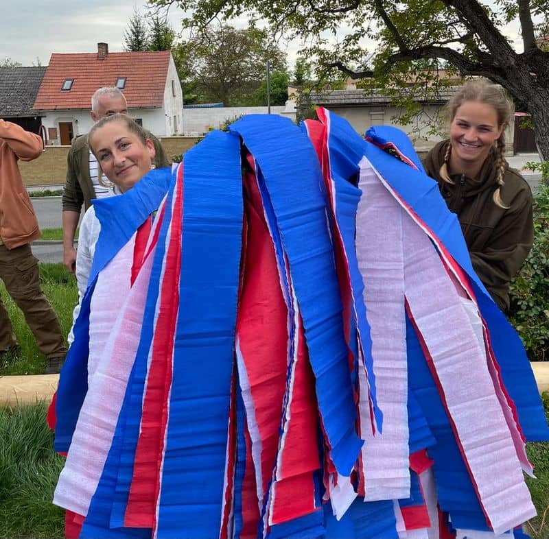 Dvě ženy zdobí májku červenými, modrými a bílými stuhami