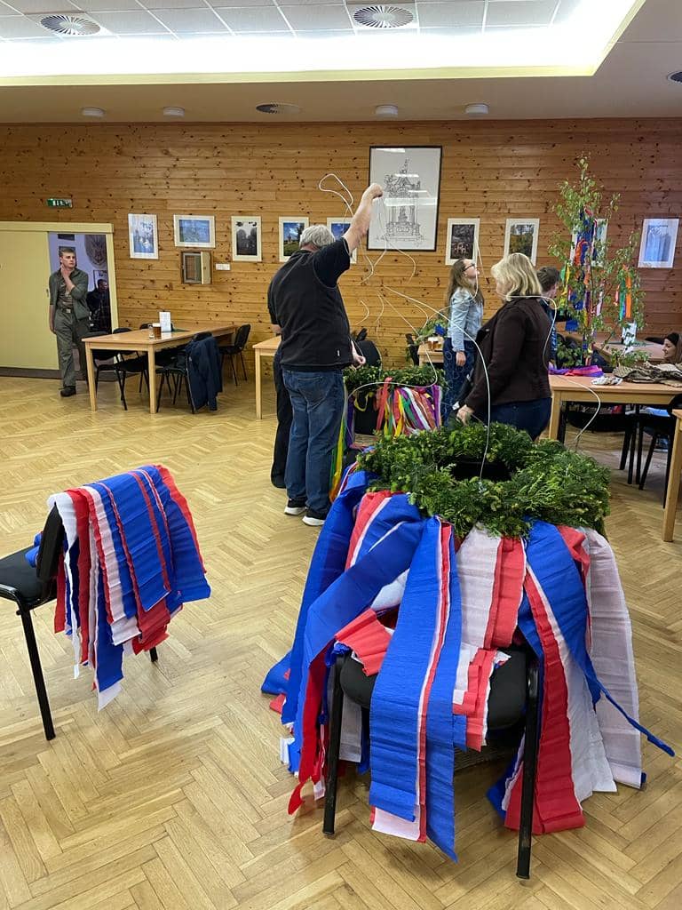 Skupina lidí zdobí májku a věnce v sále