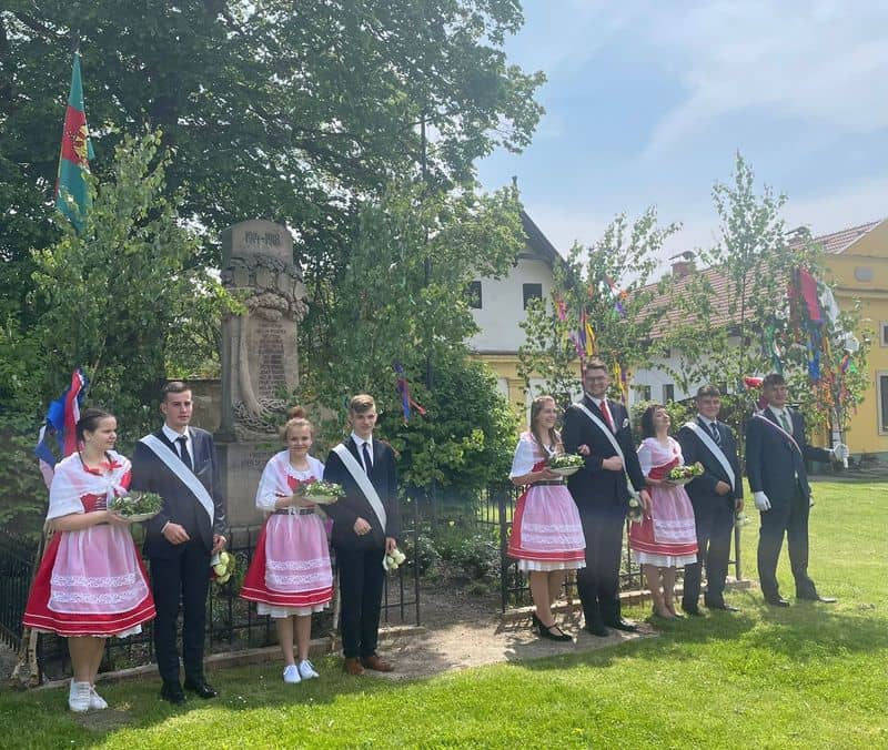 Skupina mladých lidí v krojích a oblecích u pomníku padlých