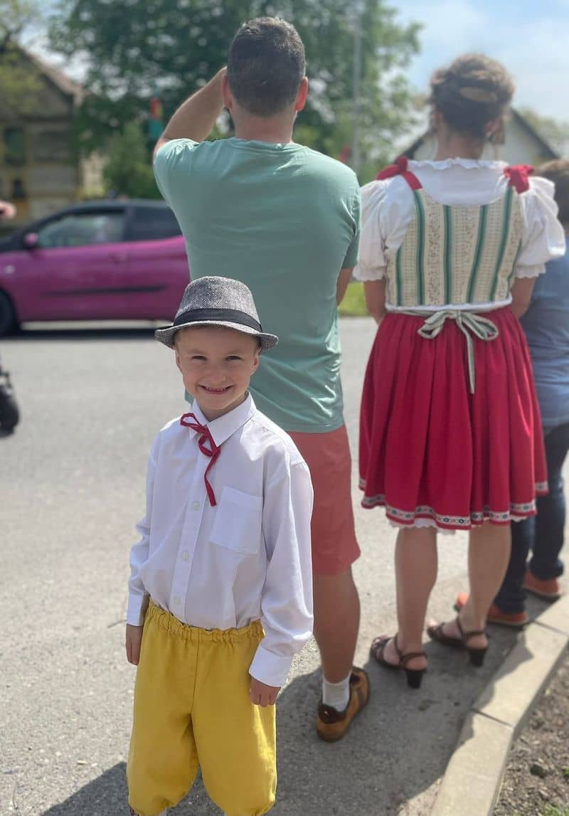 Chlapec v kroji s kloboukem, za ním dospělí