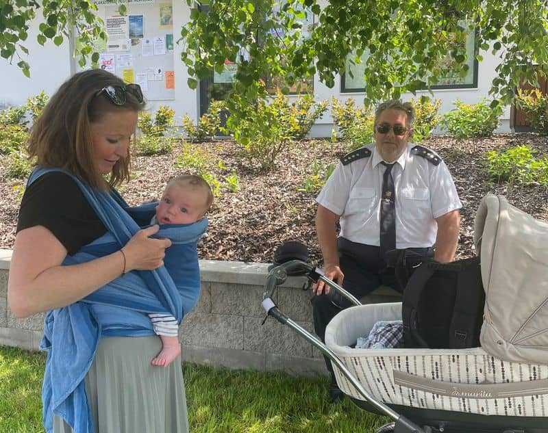 Žena s dítětem v šátku a muž v uniformě sedící u kočárku