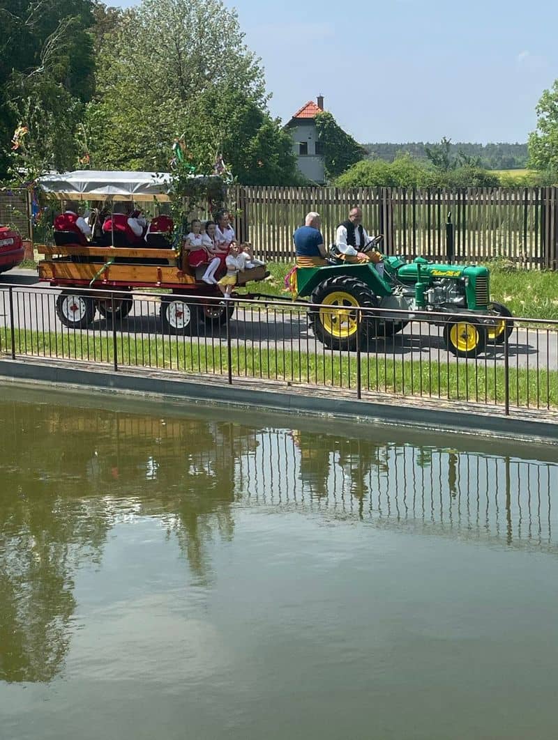 Zelený traktor táhne vůz s lidmi v krojích