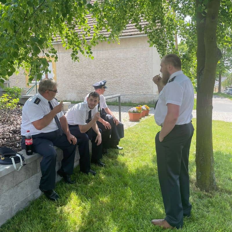 Skupina mužů v uniformách odpočívá ve stínu stromu