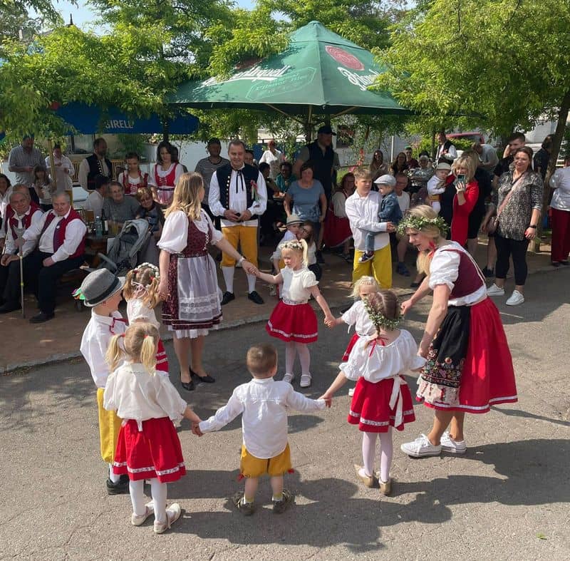 Děti a dospělí v krojích tančí v kruhu, kolem nich stojí další lidé