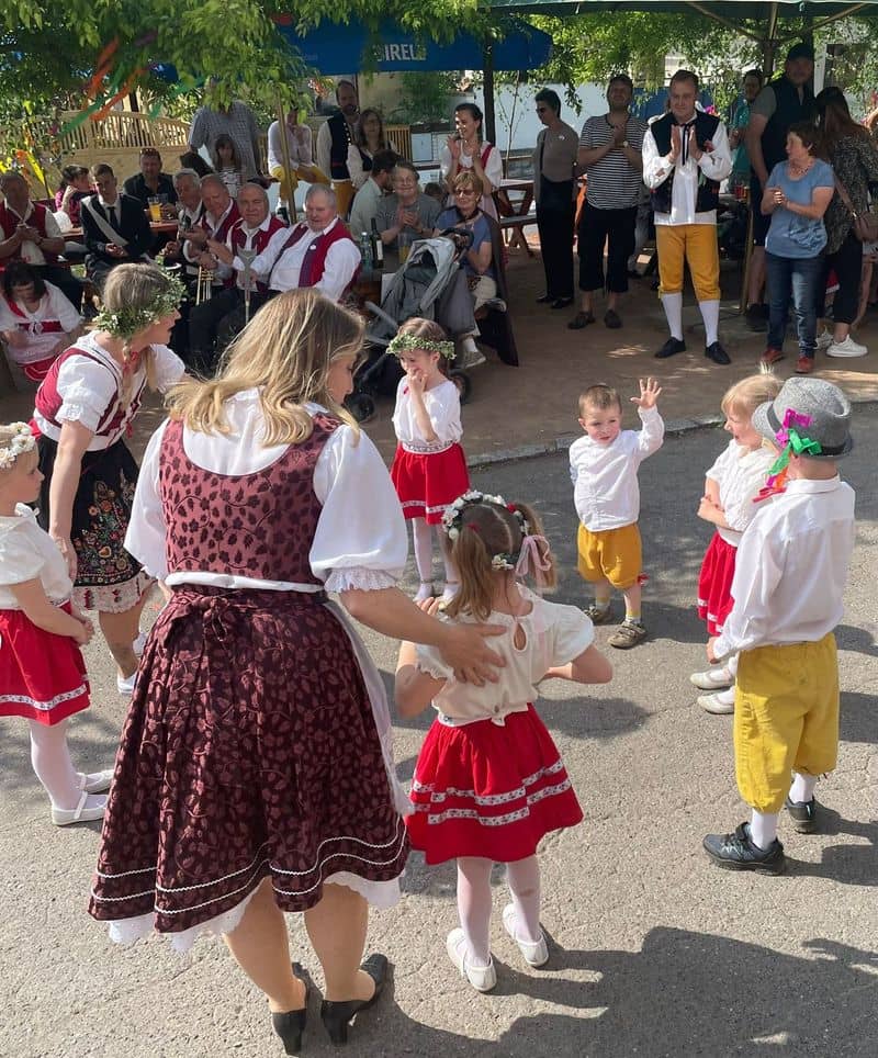Ženy a děti v krojích tančí, v pozadí přihlížejí lidé