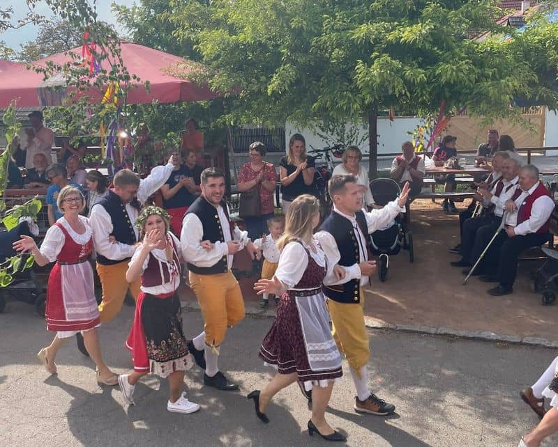 Skupina lidí v krojích tančí na ulici, diváci tleskají