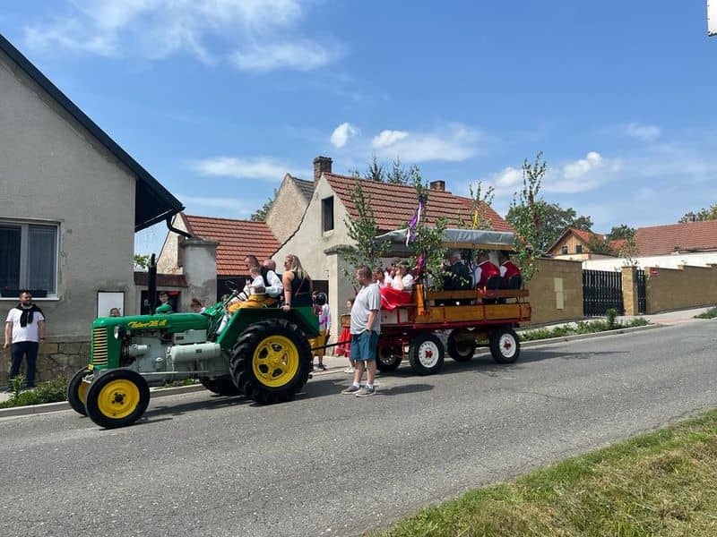 Zelený traktor Zetor 25 A táhne dřevěný vůz s lidmi v krojích