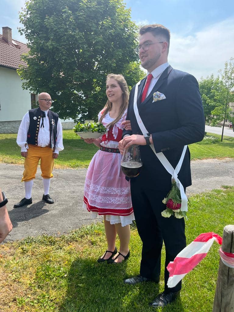 Tři lidé v krojích a obleku na venkovní slavnosti