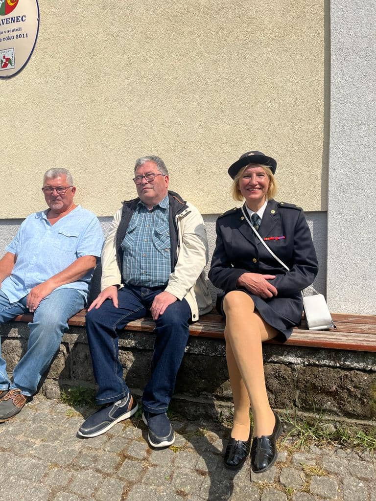 Tři lidé sedí na lavičce, žena v uniformě hasičky