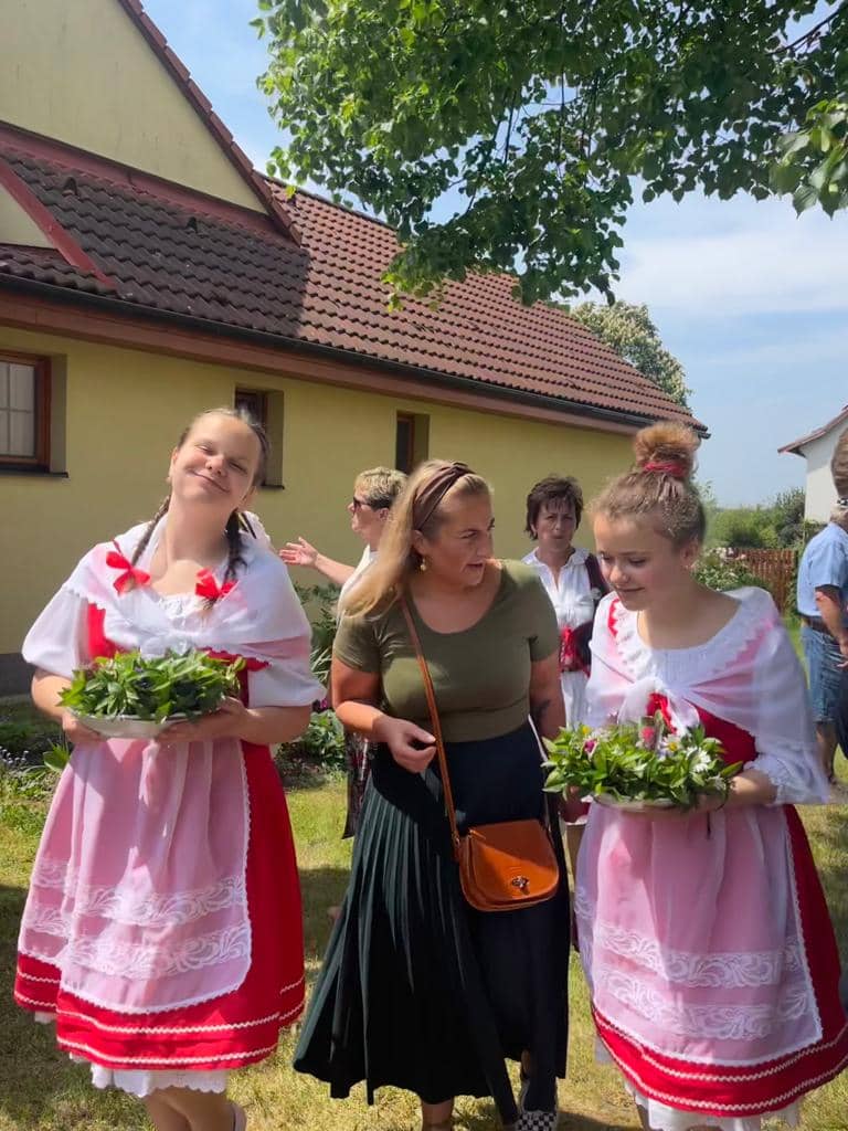 Dvě dívky v krojích drží misky s bylinkami, za nimi skupina žen