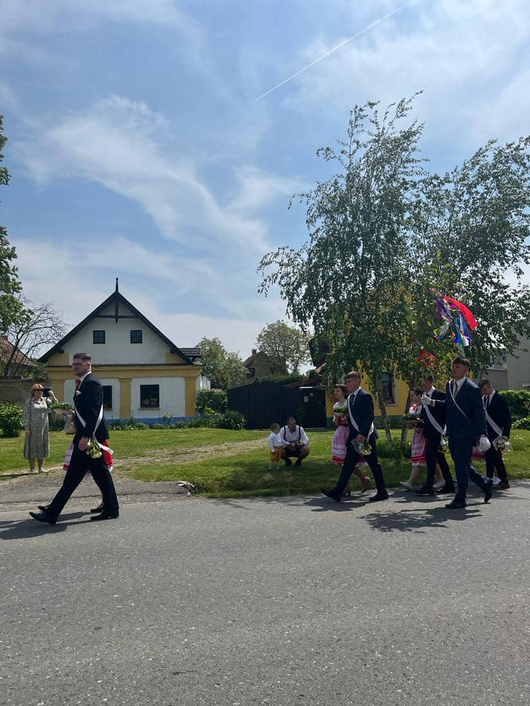 Průvod mužů v oblecích a žen v krojích na ulici